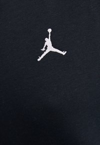 Silhouette d'un joueur de basket sautant, un bras tendu tenant un ballon, brodée en blanc sur tissu noir.