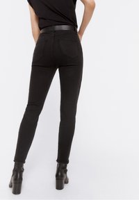 Černé skinny džíny s vysokým pasem, dvěma zadními kapsami a roztrhanými lemy, doplněné černými kotníkovými botami. Hladká denním texturu.