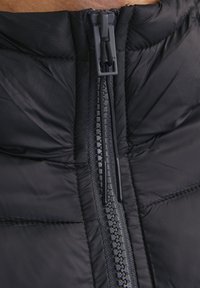 Black insulated jacket close-up featuring a durable zipper along the front, quilted texture, and elastic drawstring at the collar.