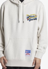 Kremowa bluza z kapturem z przednią kieszenią, z kolorowym graficznym logo i naszywką w dolnej lewej części. Wykonana z miękkiej tkaniny, o luźnym kroju.