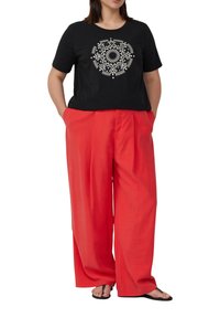 Zwarte katoenen t-shirt met witte geometrische print, gecombineerd met losse rode broek. De broek heeft een tailleplooitje en zijzakken.