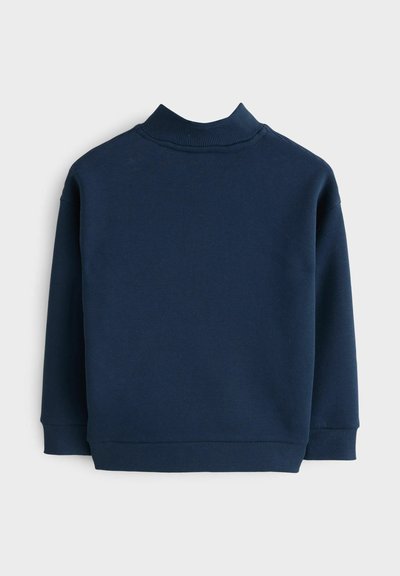 Tumši zila džemperis ar ribotu augstu apkakli, garām piedurknēm un gludu tekstūru. Tajā ir vienkāršs, nepārtērēts dizains, kas piemērots kā kārtiņš apģērbā.