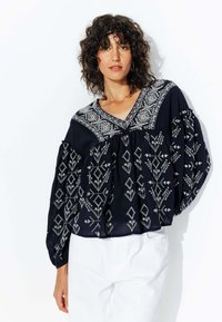 Blouse bleu marine avec broderie florale blanche, décolleté en V et manches ballons, présentant un design froncé et des détails élaborés sur le corsage.