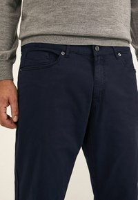 Pantalones de algodón azul marino con corte recto, con cierre de botón, bolsillos frontales y una textura sutil.