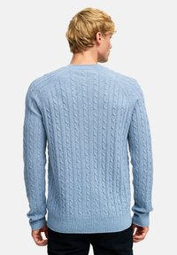 Jasnoniebieski sweter w warkocze z podwójnym ściągaczem przy mankietach i u dołu. Charakteryzuje się fakturowanym wzorem z wyraźnymi splotami, dopasowaną sylwetką i okrągłym dekoltem.