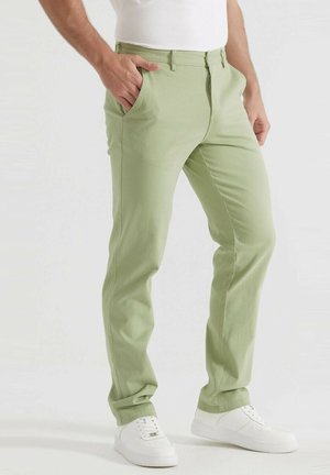 Chino en coton vert clair avec une coupe slim, deux poches latérales et une texture lisse, associés à des baskets blanches.