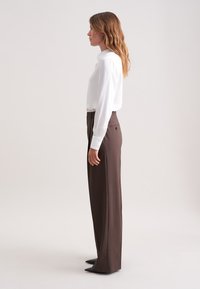 Witte blouse met lange mouwen en verticale strepen, gecombineerd met hoge, bredere bruine broek en puntige zwarte hakken.