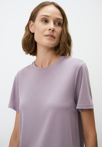 Koszulka z krótkim rękawem z miękkiej tkaniny w odcieniu liliowym, z klasycznym okrągłym dekoltem i luźnym krojem, o gładkiej teksturze i minimalnych detalach szwów.