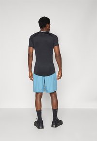 Black fitted athletic shirt with short sleeves, paired with light blue shorts. The shirt has a curved hem and branded neckline.