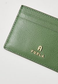 Porte-cartes en cuir vert avec une finition texturée, doté de quatre fentes pour cartes et d'un logo doré embossé "FURLA" sur le devant.
