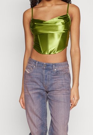 Personne portant un haut court en satin vert olive brillant à bretelles spaghetti et un jean violet délavé taille haute.