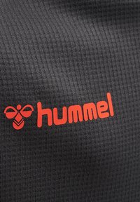Donkergrijze textuurstof met verticale ribbels, met een prominent rood "hummel" logo en een cirkelvormig logo-ontwerp erboven.