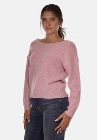 Maglione rosa a maglia con scollo rotondo, spalle cadenti e orlo a coste. Texture morbida con delicati accenti glitterati. Indossato con jeans scuri.