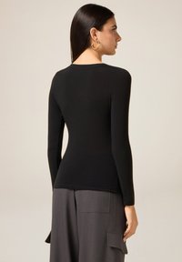Czarna bluzka z długim rękawem wykonana z miękkiego, elastycznego materiału o dopasowanym kroju i okrągłym dekoltem, zestawiona z szarymi spodniami z wysokim stanem.