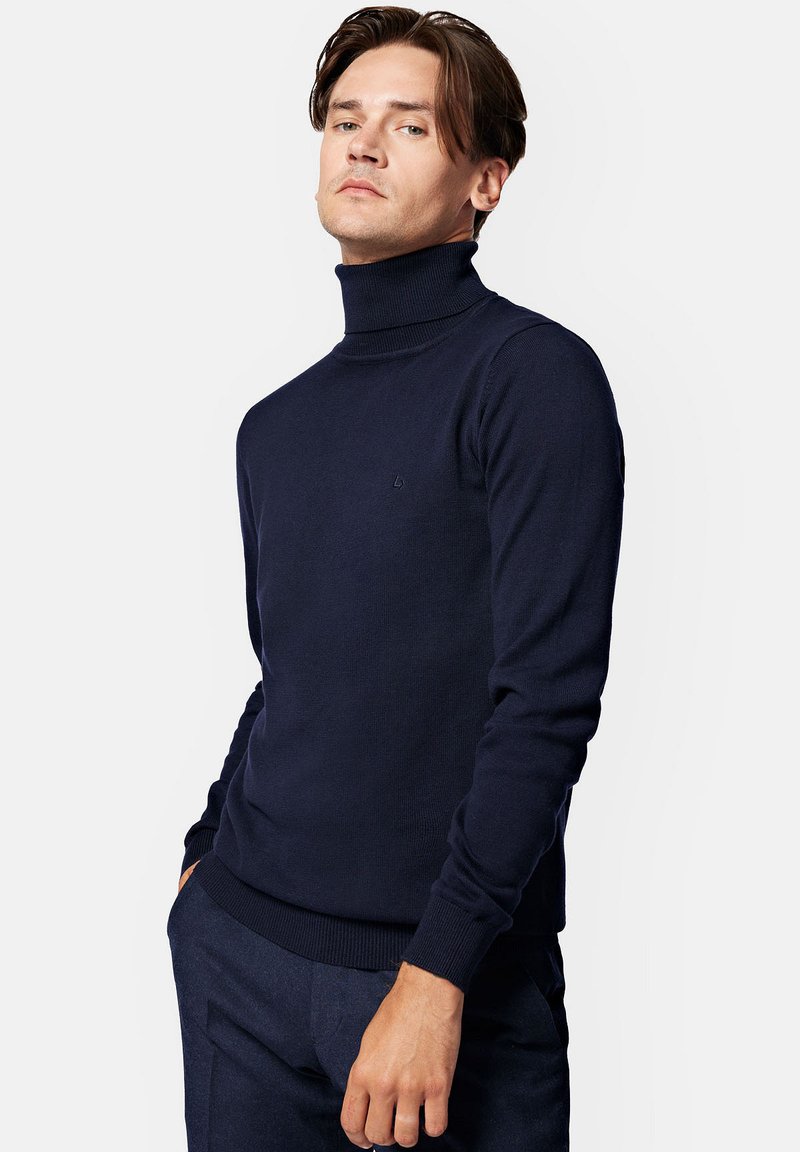 Granatowy sweter z golfem z miękkiej dzianiny, z długimi rękawami oraz ściągaczami na rękawach i u dołu. Dyskretna logo na klatce piersiowej.