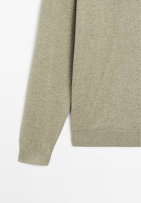 Oliven grøn strikketrøje med rund halsudskæring, ribbede manchetter og søm. Teksturen er blød med en glat finish og minimal mønstring.
