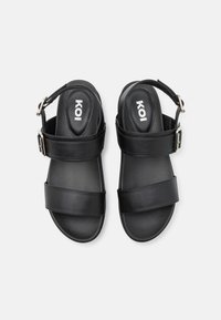 Black sandals with two wide straps and a back ankle strap. Made of smooth material, featuring a silver buckle accent.