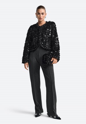 Schwarze, flauschige, paillettenbesetzte Jacke über enganliegenden grauen Hosen, kombiniert mit einer passenden Clutch und spitzen Schuhen mit Verzierungen.