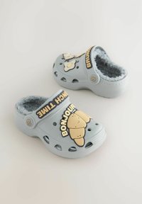 Light blue clogs with a soft fur lining, featuring a smiling croissant and "BONJOUR BRUNCH TIME" text in bold, black letters.