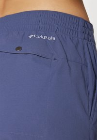 Columbia blå shorts med elastisk talje, en frontlomme med knap og en glat stofstruktur. Logo synligt på taljen.
