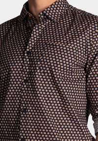 Navyblauw overhemd met knopen en een klein bloemenpatroon in crème. Voorzien van een puntkraag, borstzak en een gestructureerde stof.