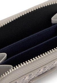 Szara pleciona kopertówka z zamkiem błyskawicznym, z wnętrzem wyposażonym w dwie granatowe tkaninowe przegródki i srebrne elementy ozdobne.
