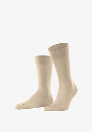 Beige cotton socks with a smooth texture, mid-calf length, and ribbed cuff, featuring minimal design and a small logo on the sole.