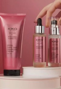 Tre prodotti per capelli di KIKO Milano: un tubetto di crema rosa, una bottiglia di olio in vetro con contagocce e una bottiglia spray con dettagli argentati su un piedistallo.