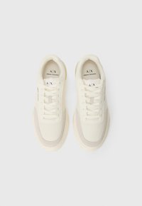 White sneakers with mesh fabric, rubber soles, and beige accents. Features laces and a logo print on the side. Cushioned collar.