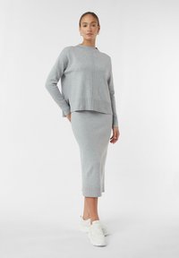 Maglione lavorato a maglia grigio chiaro con scollo a giro e spacchi laterali, abbinato a una gonna coordinata al ginocchio. Sneakers bianche completano l'outfit.