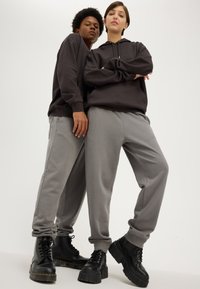 Deux mannequins portant des sweat-shirts à capuche sombres et des pantalons de survêtement gris. Des bottes à plateforme lacées noires avec des semelles épaisses. Coupe athlétique et ajustement décontracté.