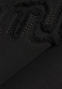 Čierna látka s rebrovou textúrou, s prešívanými detailami a chlpatým vzorom. Detailný pohľad na materiál a šitie.