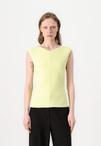 Lys grønn ermeløs topp med et teksturert, skrå ribbestruktur, med V-hals og en tettsittende silhuett. Kombinert med svarte bukser.