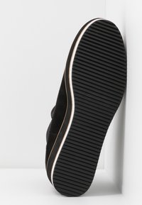 Czarny zamszowy spód buta z teksturowaną gumową podeszwą, z białym konturem i żłobieniami dla lepszego uchwytu. Umieszczony na jasnym tle.