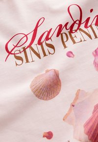 Tissu rose clair avec le texte "Sandini Sinis Penins" en rouge et marron, agrémenté d'illustrations de coquillages éparpillées dans des teintes douces.