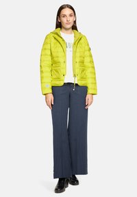 Jasnozielona puchowa kurtka z kapturem, zapinana na zamek, z dwoma przednimi kieszeniami. Nosi się ją na białą bluzkę i granatowe spodnie w prążki.
