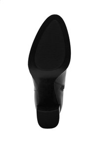Suela de zapato negra con superficie lisa, forma ligeramente puntiaguda y ranuras texturizadas para tracción. Sin marcas ni acentos visibles.