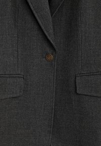 Blazer en laine gris foncé avec revers cranté, un bouton décoratif doré et deux poches à rabat à l'avant.