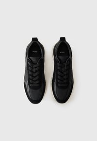Svarte sneakers med en glatt lær- og tekstiloverdel, med avrundet tå, seks snøringshull og en kontrasterende gummisåle.