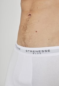 Boxers blancs en tissu doux, avec une ceinture élastique marquée en noir et gris portant l'inscription "STRENESSE BLUE" en évidence.
