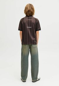 Camisa negra a rayas de manga corta con un collar alto, combinada con unos vaqueros verdes desgastados y holgados. Diseño simple con un texto sutil en la parte posterior de la camisa.