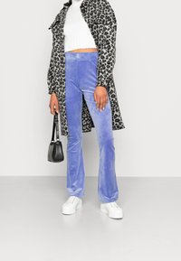 Lila sammetsbyxor med utsvängd ben, i kombination med en ribbad vit crop top och en leopardmönstrad kappa, kompletterat med en svart handväska och vita platåskor.