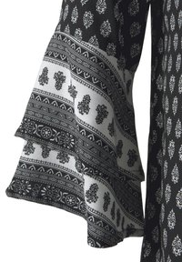 Blouse à motifs noir et blanc avec des manches évasées, des designs floraux et géométriques complexes, un tissu doux et des détails de ourlet superposé.