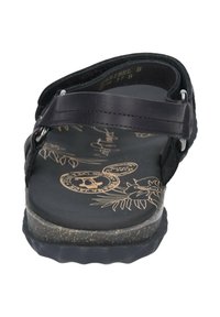 Svart sandal med en texturerad svart ovandel och en bärbar fotbädd med tryck i tan, med en böjd sula och metallaccent på remmarna.