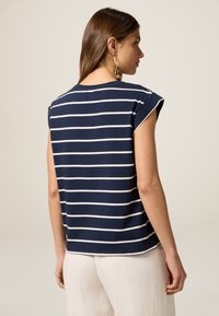 Top de corte relajado azul marino con rayas horizontales blancas, mangas cortas y cuello redondo. Tela suave con un diseño limpio y moderno.