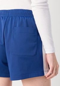 Calções de desporto azuis com um acabamento texturizado, apresentando um bolso traseiro e detalhes brancos nas laterais. A cintura é elástica para um ajuste seguro.