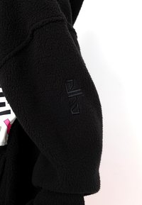 Schwarze Fleecejacke aus strukturiertem Stoff mit einem dezenten gestickten Logo auf dem Ärmel und einem kontrastierenden grafischen Design auf dem Körper.