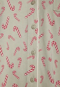 Lys beige skjorte med et gjentakende mønster av røde og hvite sukkertøystokker, pyntet med lyse knapper langs frontåpningen.