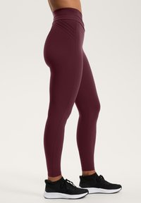 Leggings bordo cu talie înaltă, cu o textură netedă și un design pliat la talie, asortate cu adidași negri.