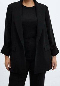 Sort blazer lavet af glat stof med et skræddersyet design, beklædning med hakkede revers og op rullede manchetter. Båret over en matchende sort top.